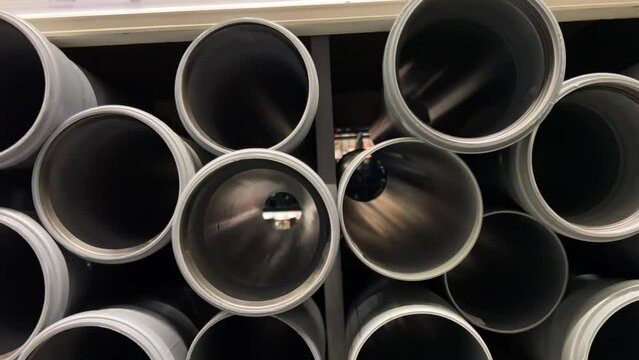 Close-up front view of a rows of plastic water pipes stacked on a shelf in a hardware store. The pipes are of different sizes, diameters. They are made of high-quality plastic
