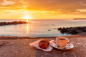 cup of coffee or tea with croissant on a morning embarkment beach with blue sea and beautiful...