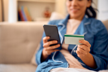 Close up of woman online banking with smart phone and credit card at home,