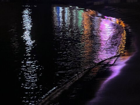 Night sea waves on the sand beach with colorful light reflections.
