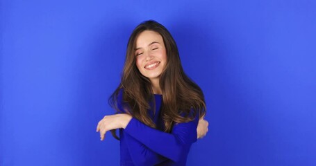 Come into my arms. Adorable happy girl with brown hair in blue long sleeves gesturing come here for free hugs and smiling sincerely with welcoming expression isolated on blue background. Come to me!