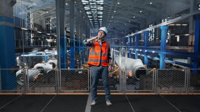 Full Body Of Asian Male Engineer With Safety Helmet Standing In Factory Manufacture of Wind Turbines. Showing Thumbs Down Gesture And Shaking His Head While Robotic Arm Working