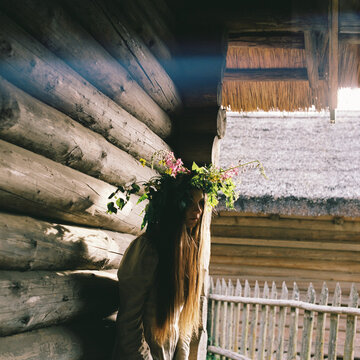 The girl is standing at the house with a wreath on her head.