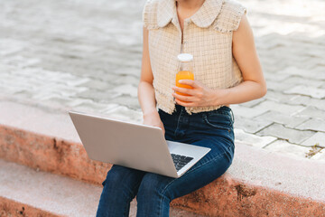  asian woman sits on stairs of university campus and drinks