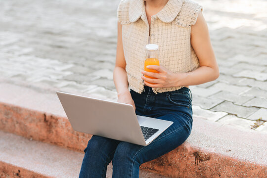  asian woman sits on stairs of university campus and drinks