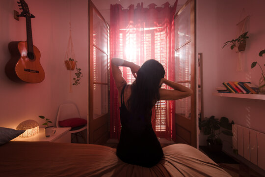 Woman waking up in bedroom with bright sunlight window