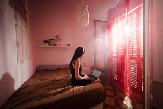 Focused woman using laptop and headset in bedroom