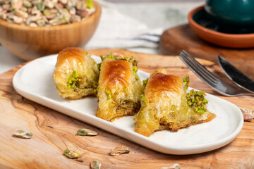 Pistachio şöbiyet baklava. Turkish and Arabic cuisine delicacies. Şöbiyet baklava with clotted cream and pistachios on a wooden presentation plate. Close up
