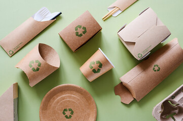 Disposable tableware made from recycled cardboard on a green background. Food packaging with green recycling signs.