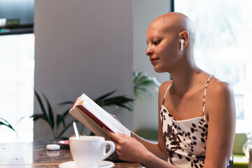 Young hairless woman drinking coffee and reading novel in cafete
