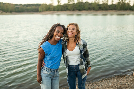 Portrait of two amigas embracing on the bank of a river in nature.