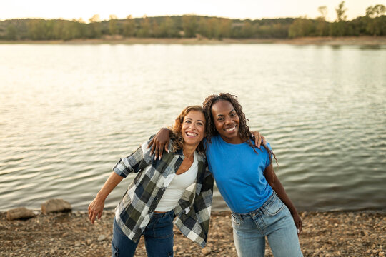 Portrait of two amigas embracing on the bank of a river in nature.