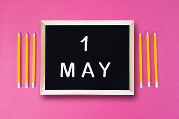 May 1 written in chalk on black board. Calendar date 1st of May on chalkboard on pink blurred...