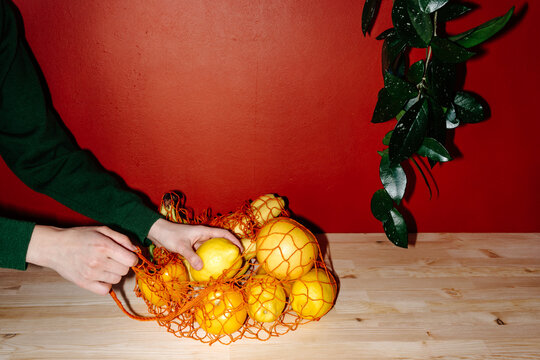 Direct flash, crop person taking lemon from mesh bag with groceries