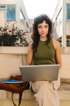 Smiling young studious woman studying with laptop outdoors