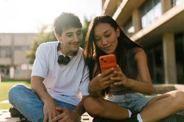 Cheerful multiethnic young students using smartphone on street