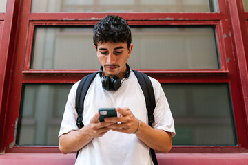 Young Hispanic man surfing smartphone for text messages