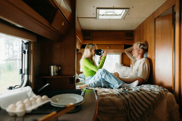A woman takes pictures of a man sitting on a bed in a van