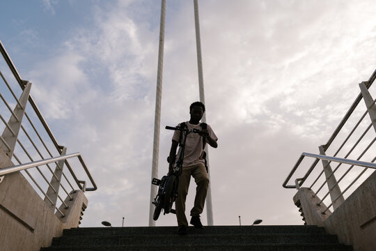Black man carrying e bicycle on stairs