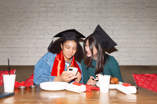 Diverse graduates using smartphone in cafe