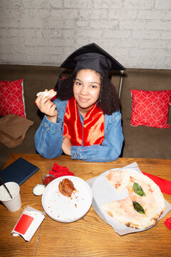Smiling black girl eating pizza after graduation