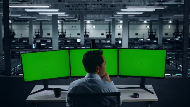 Back View Of Asian Man Thinking About Something While Working With Mock Up Multiple Computer Monitor In Data Center