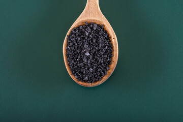 Distinctive Contrast: 4K Ultra HD Image of Black Salt in Wooden Spoon on Green Background