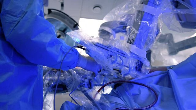 Cooperation of male surgeon and robotic surgical system. Doctor holds the tool while manipulative arm moves in patient's body.