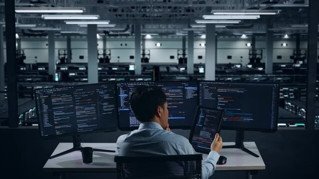 Back View Of Asian Man Developer Working With Tablet While Write Code With Multiple Computer Screens In Data Center