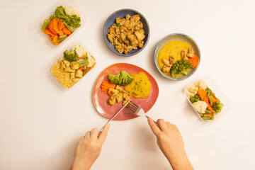 Healthy meal with chicken, manioc, broccoli being eaten by hands with fork and knife in aerial view