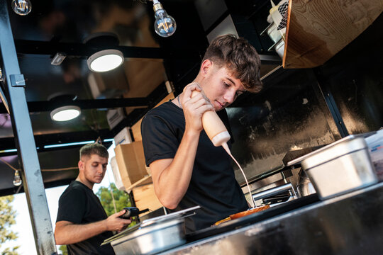 Young Chef Garnishing Dish in Urban Food Truck, Evening Service