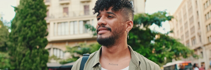 Fototapeta premium Young happy man with beard dressed in an olive-colored shirt walks along the street of the old city, looks to the side, Panorama