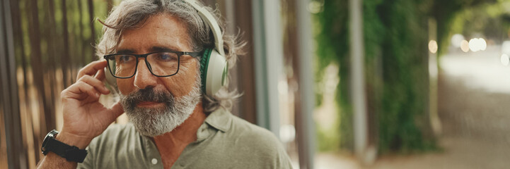 Panorama of friendly middle-aged man with gray hair and beard wearing casual clothes listening to...