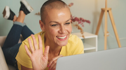 Woman dressed in yellow T-shirt and jeans talking on video call with laptop in living room