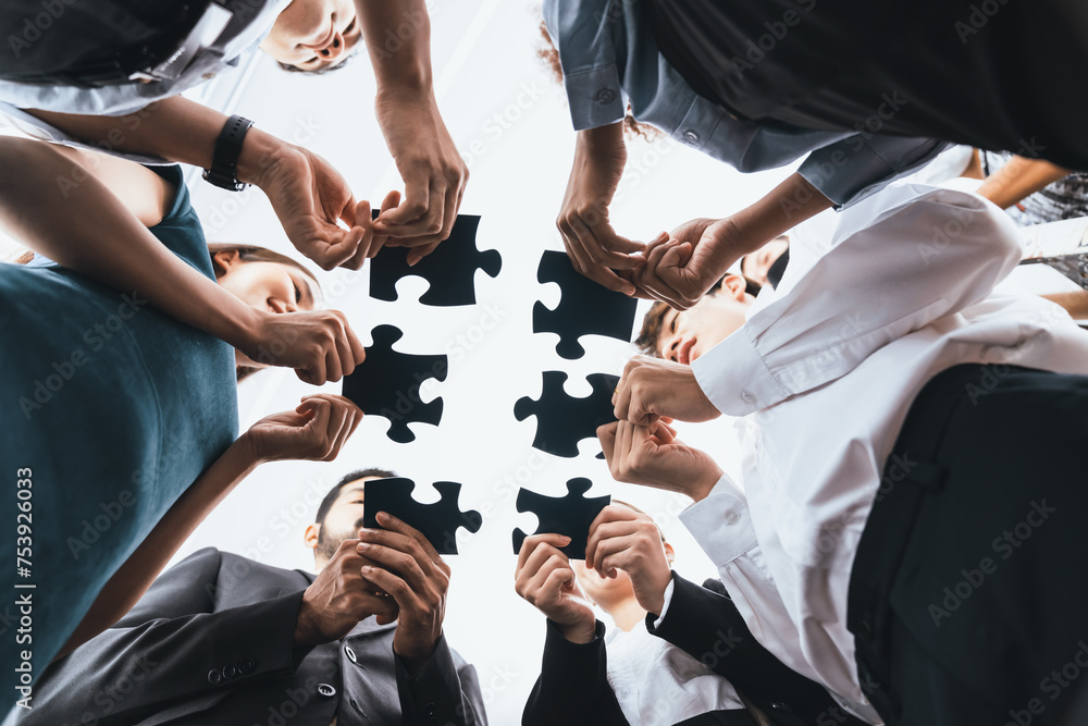Poster below view of diverse corporate officer workers collaborate in office connecting puzzle pieces as pa