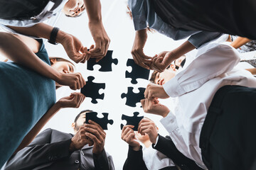 Below view of diverse corporate officer workers collaborate in office connecting puzzle pieces as partnership and teamwork concept. Unity and synergy in business idea by merging jigsaw puzzle. Concord - obrazy, fototapety, plakaty