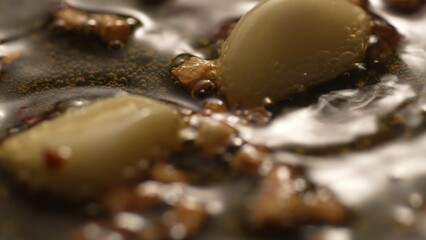 Garlic sizzling in oil in a pan. Step of Recipe Fried Assassin's Spaghetti Cooking. Close-up, shallow dof.