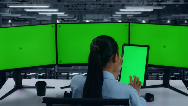 Back View Of Asian Woman Working With Tablet And Multiple Computer Monitor With Mock Up Green Screen In Data Center