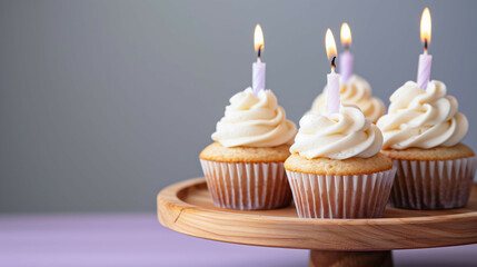 Vanilla cupcakes with white frosting and lit candles on a wooden cake stand.