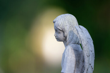 sad looking little angel figure on a gravestone in front of a beautiful bokeh