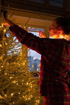 woman in red pajamas decorate Christmas tree with twinkle lights home