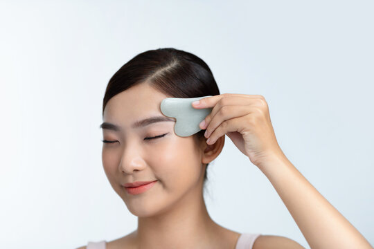 Woman smiling as she massages her face with a gua sha stone
