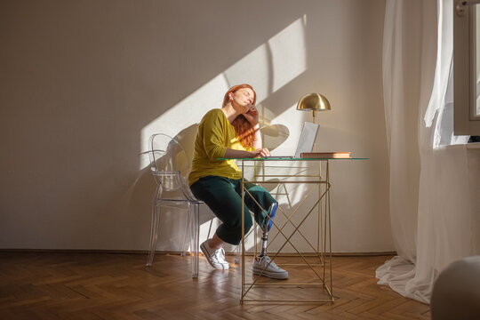 A bright woman with a prosthetic leg enjoys the sun in her home office