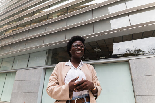 Cheerful black businesswoman standing near glass building in cit