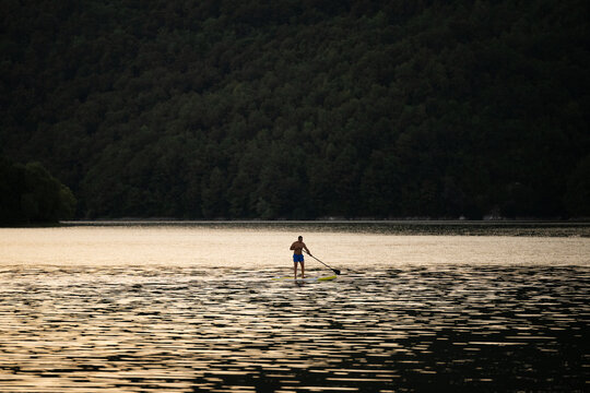 Young adult stand up paddleboarding (SUP) in a lake at sunset