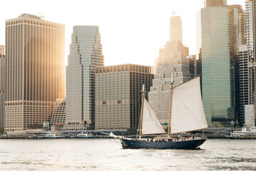 Sailboat passing by Manhattan skyline at the sunset