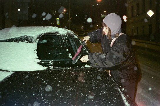 Woman removing snow from car window with hand brush at cold evening