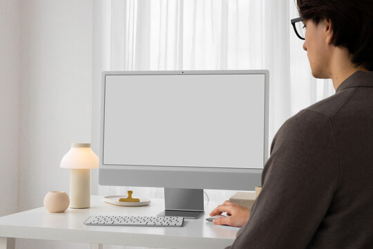 A young man is working at a computer in a bright white office