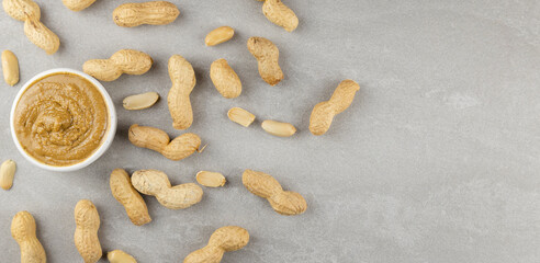 Fototapeta na wymiar Top view. Scattered raw peanuts and a jar of peanut butter on a gray background.