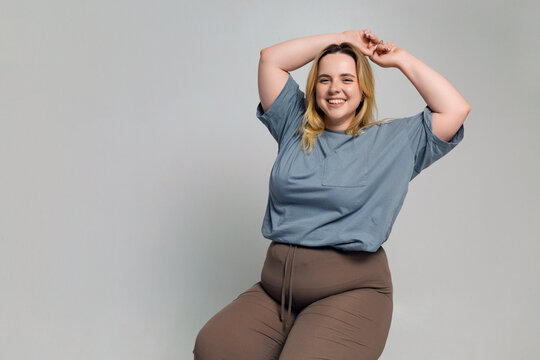 Happy young plus size woman sitting in room with gray backdrop